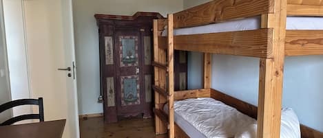 A bunk bed with a wooden frame and white bedding, a wooden table with a chair, and a door with floral decorations.