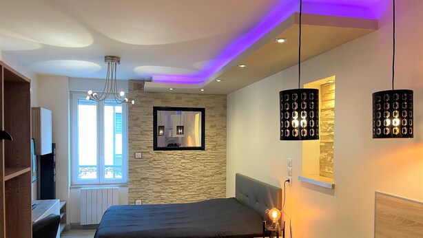 A modern bedroom with a bed, bedside table, and a desk. There is a window with a view of the outside.