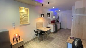 A modern kitchen with a dining area, wooden flooring, pendant lights, and a built-in wooden wall feature.