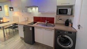 A compact kitchen with a dishwasher, washing machine, microwave, and a red backsplash.
