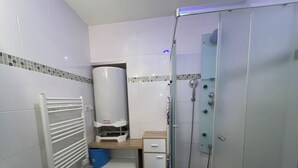 A compact bathroom with a white toilet, a sink, a shower with a glass door, and a built-in heater.
