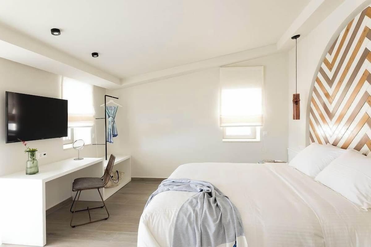 A modern hotel room with a bed, a desk, a TV, and a large window.