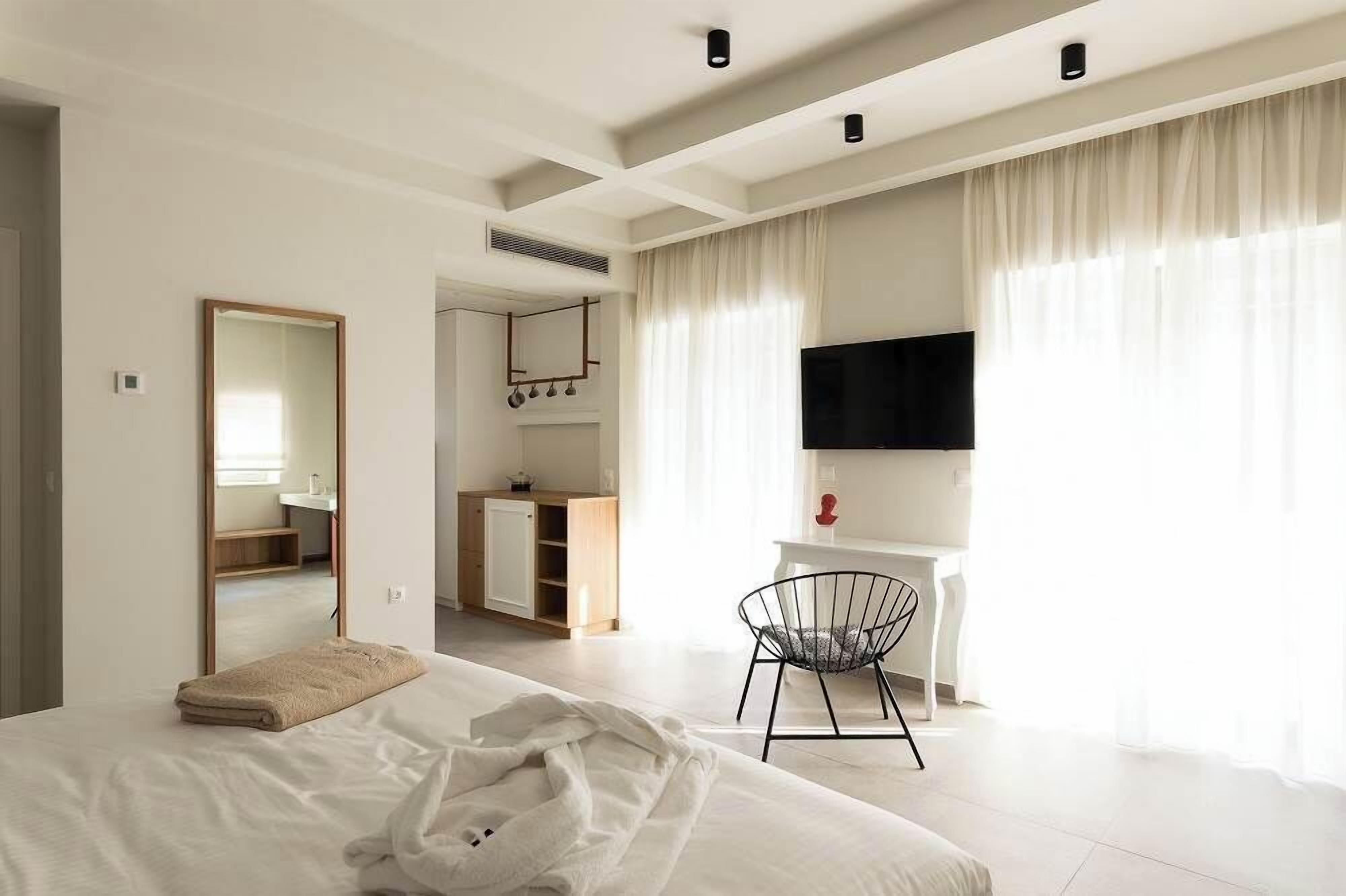 Quarto de hotel moderno com uma cama grande, uma escrivaninha, uma cadeira, uma televisão e um espelho.