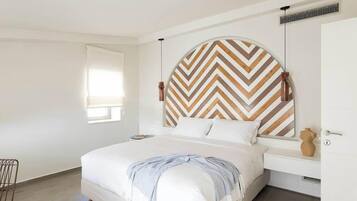 A modern bedroom with a large bed, a wooden chevron-patterned headboard, a bedside table, and a window with blinds.