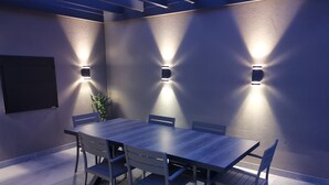 Una sala de conferències amb una taula llarga i sis cadires, tres llums penjants a la paret i una planta en test.