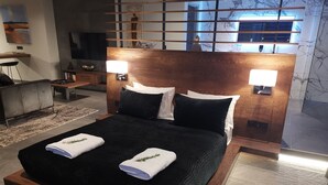 Un dormitori modern amb un llit gran, un panell de fusta al capçal, dues làmpades de nit i una vista de la ciutat a través d'una finestra.