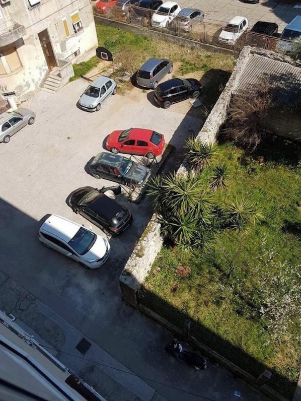 A parking lot with several cars parked, a building with a visible entrance, and some greenery.