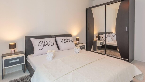 Une chambre moderne avec un grand lit, deux tables de chevet avec des lampes, une armoire et un miroir.