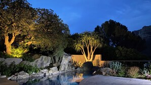 Un espace extérieur avec piscine, aménagé pour la nuit, comprenant une formation rocheuse, des arbres et un ciel dégagé.