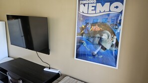 Een flatscreen televisie aan een muur, een poster van Zoek de Vis, en een bureau met een stoel.