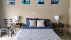 Een slaapkamer met een bed, twee nachtkastjes, een stoel en wanddecoratie met zeeschildpadden.
