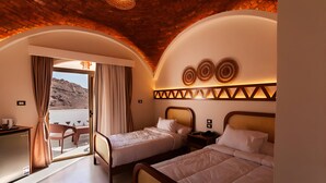 Ein Hotelzimmer mit zwei Betten, einem Schreibtisch und einem Balkon mit Vorhängen.