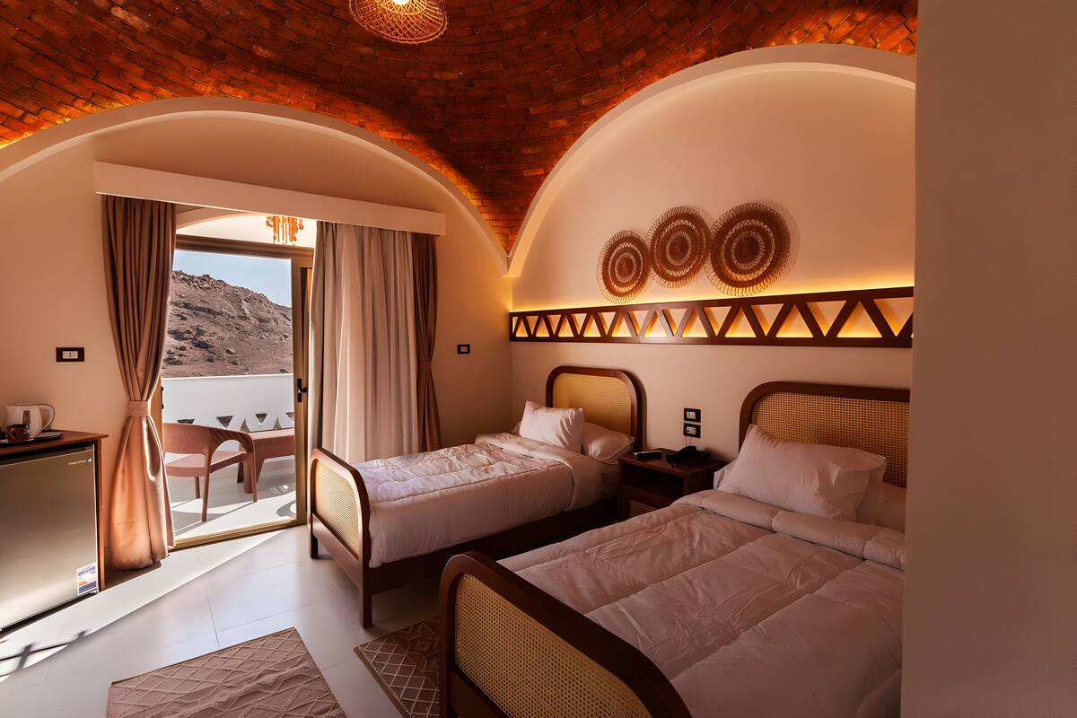 Habitación de hotel con dos camas, un escritorio y un balcón con cortinas.