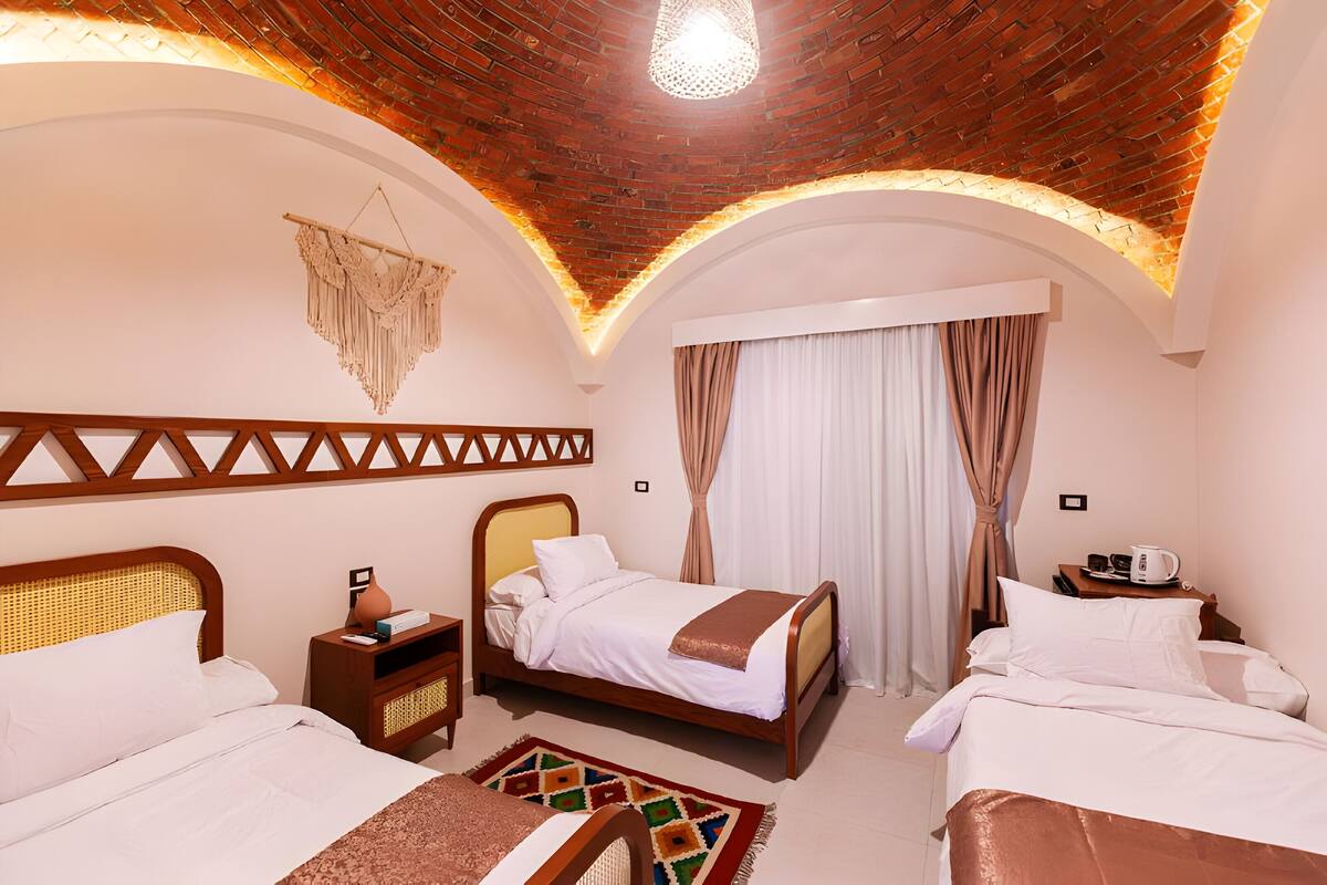 Habitación de hotel con dos camas, cabecera de madera, tapiz tejido en la pared y lámpara en el techo.