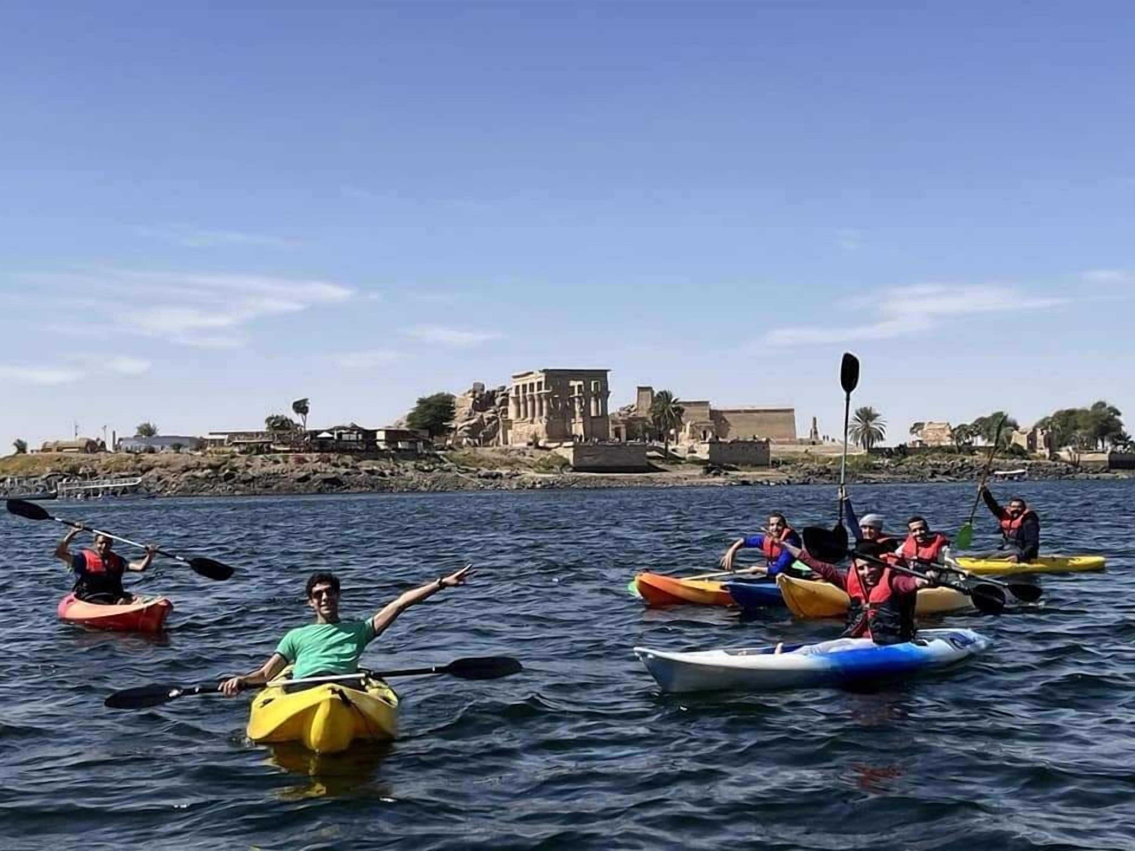 Un groupe de personnes pratiquant le kayak sur une étendue d’eau calme, avec un bâtiment historique en arrière-plan.