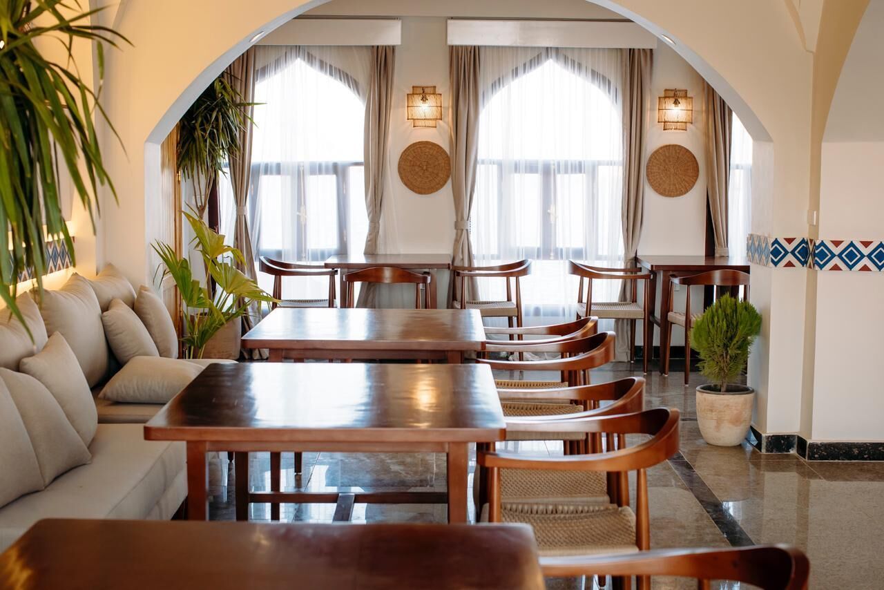 A dining area with a long wooden table and chairs, a sofa, and a potted plant.