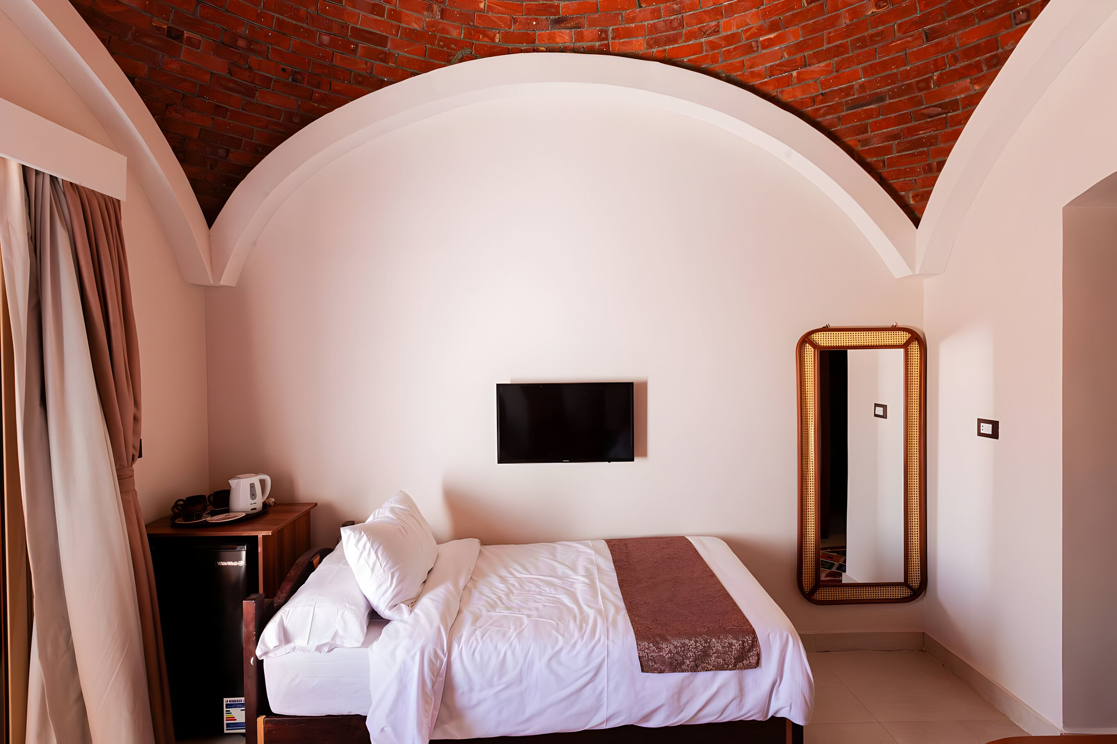 Un dormitorio con techo de ladrillo, una cama con ropa de cama blanca, una mesita de noche con hervidor y un espejo grande.