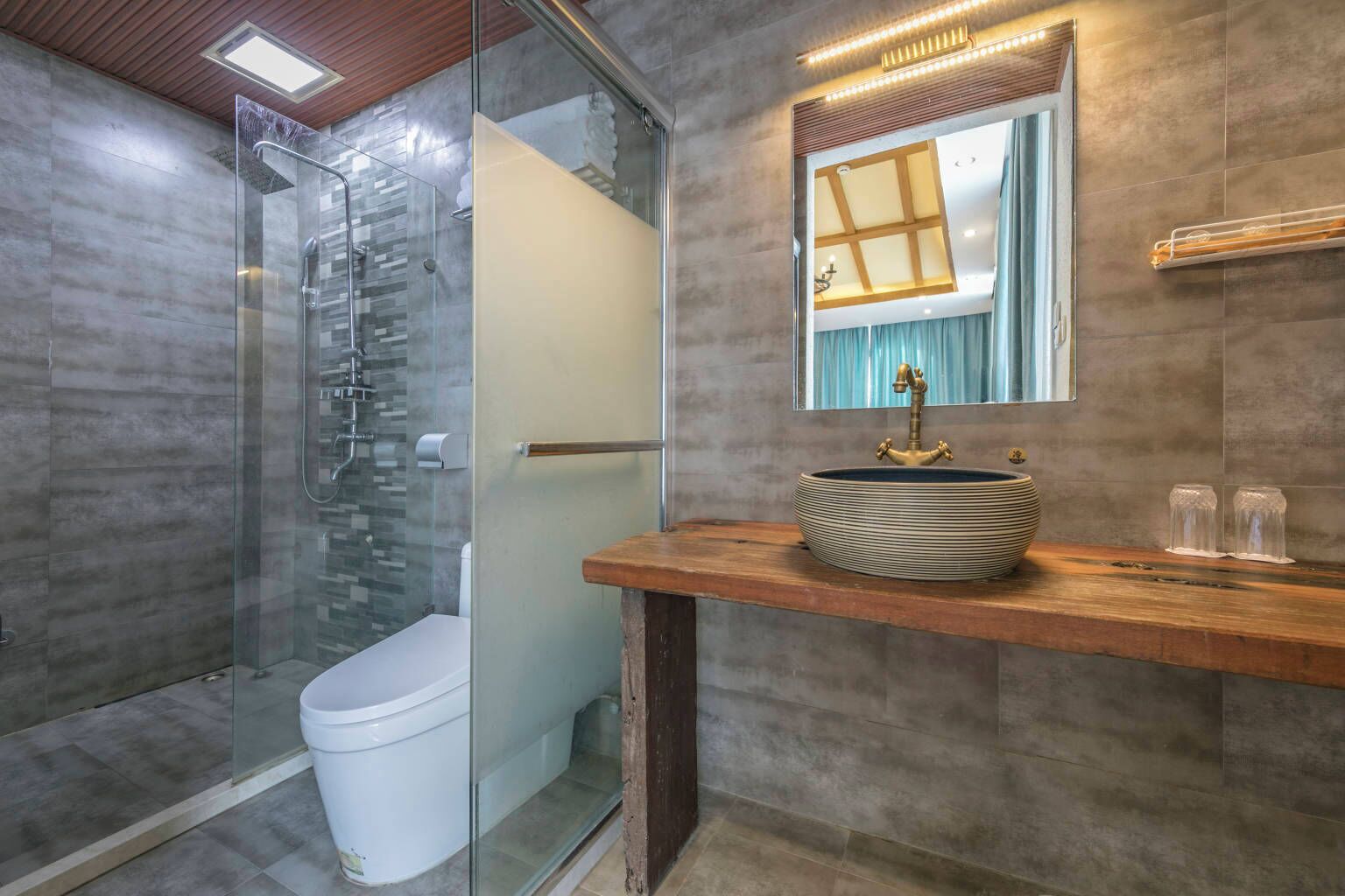 Un bagno moderno con doccia vetrata, un water bianco e un mobile bagno in legno con lavandino tondo.