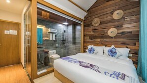 Ein modernes Hotelzimmer mit einem Holzkopfteil, einer Duschkabine aus Glas und einem Bett mit einem Zierkissen.