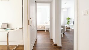 A modern, well-lit hallway with a laptop on a desk, a bed with a floral bedspread, and a dining area with a plant. - Superb flat in historic centre of Athens (Athens)