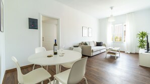 A modern living room with a round dining table, white chairs, a sofa, and a television on a stand. - Superb flat in historic centre of Athens (Athens)