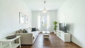 A modern living room with a sofa, a coffee table, a TV on a stand, and a potted plant. - Superb flat in historic centre of Athens (Athens)