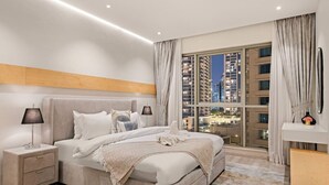 Un dormitorio moderno con una cama grande, mesitas de noche, una mesita auxiliar, vista a un paisaje urbano a través de un ventanal amplio y un cabecero de madera.