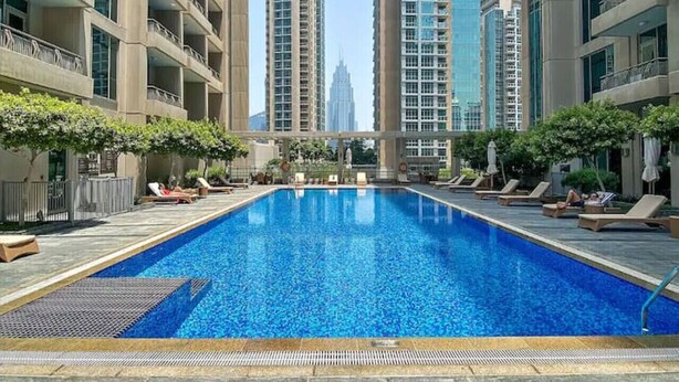 Una piscina con sillones de descanso y vistas a edificios altos al fondo.