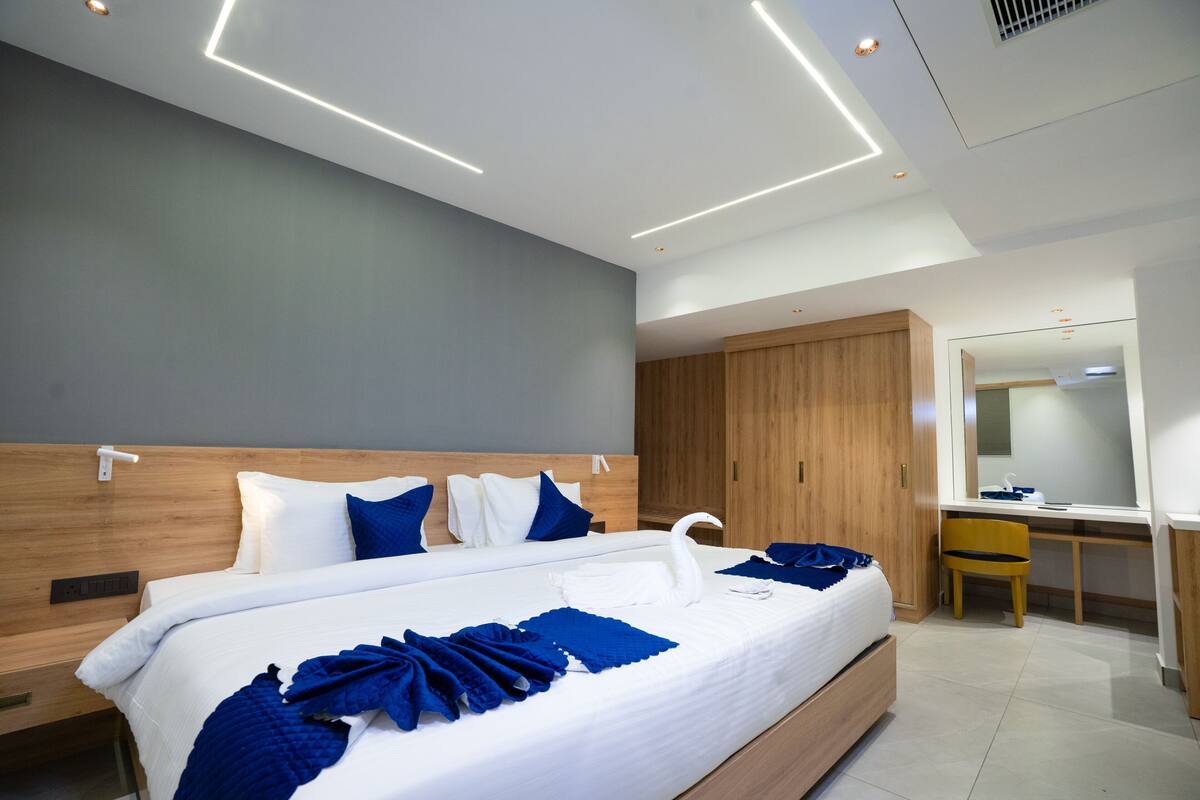 A modern hotel room with a large bed, wooden headboard, and a desk with a chair.