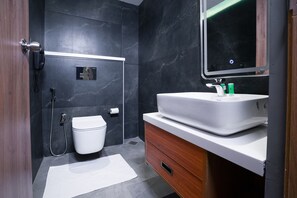 A modern bathroom with a white toilet, a sink with green toiletries, and a mirror above the sink. - Blue Moon (Ambalapuzha)
