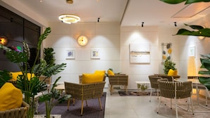 Un'area lounge moderna con mobili in vimini, cuscini gialli e piante da interno.