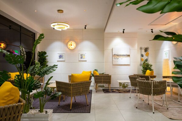 A modern lounge area with wicker furniture, yellow cushions, and indoor plants. - Blue Moon (Ambalapuzha)