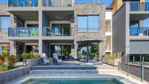Un edificio moderno a più piani con piscina, area relax all'aperto e facciata in pietra.