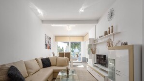 Un soggiorno moderno con un divano color beige, un tavolino in vetro e mobili contenitori bianchi.