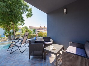 A patio with wicker furniture, a pool, and a view of buildings in the background. - Apartment in Kukci Near Spadici Beach (Porec)
