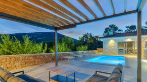 An outdoor patio with a stone wall, wooden pergola, and a swimming pool.