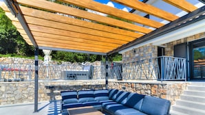 An outdoor seating area with a wooden pergola, stone walls, and a stone staircase.