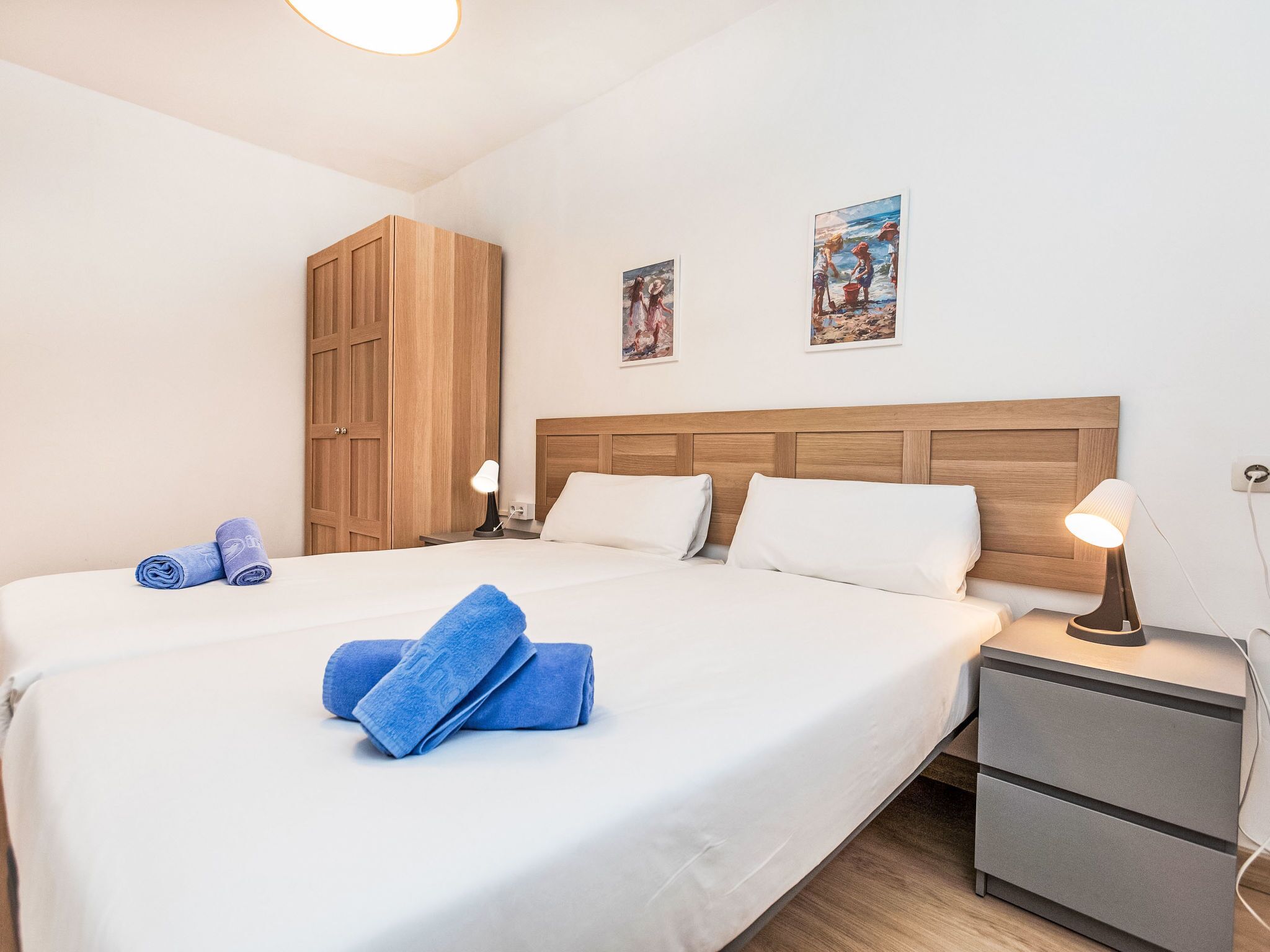 Un lit bien fait, avec des serviettes bleues, une tête de lit en bois, une table de chevet avec une lampe et une petite armoire.