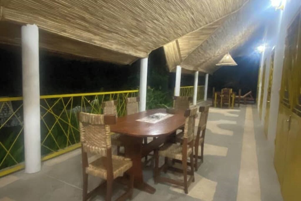 An outdoor covered dining area with a round table and chairs, surrounded by a yellow railing and a glass wall.