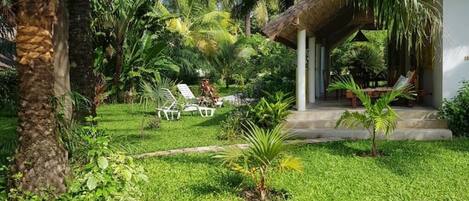 A lush garden with a thatched-roof structure, white lounge chairs, and a variety of tropical plants.