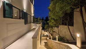 A nighttime view of a building with a staircase leading to a balcony, surrounded by trees and a stone wall.