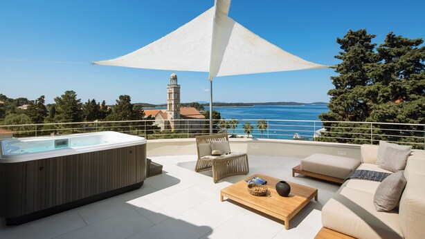 A rooftop terrace with a hot tub, seating area, and a view of the sea and a church.