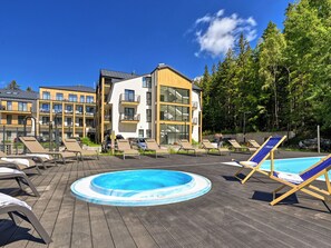 A pool area with lounge chairs and a hot tub, surrounded by multi-story buildings with balconies.