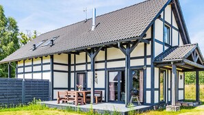 Een traditioneel vakwerkhuis met schuin dak, een veranda met houten banken en een barbecue buiten.