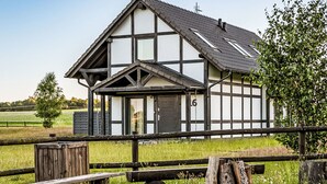 Een traditioneel vakwerkhuis met een puntgevel, met het nummer '6' duidelijk zichtbaar aan de zijkant, en een houten omheining op de voorgrond.