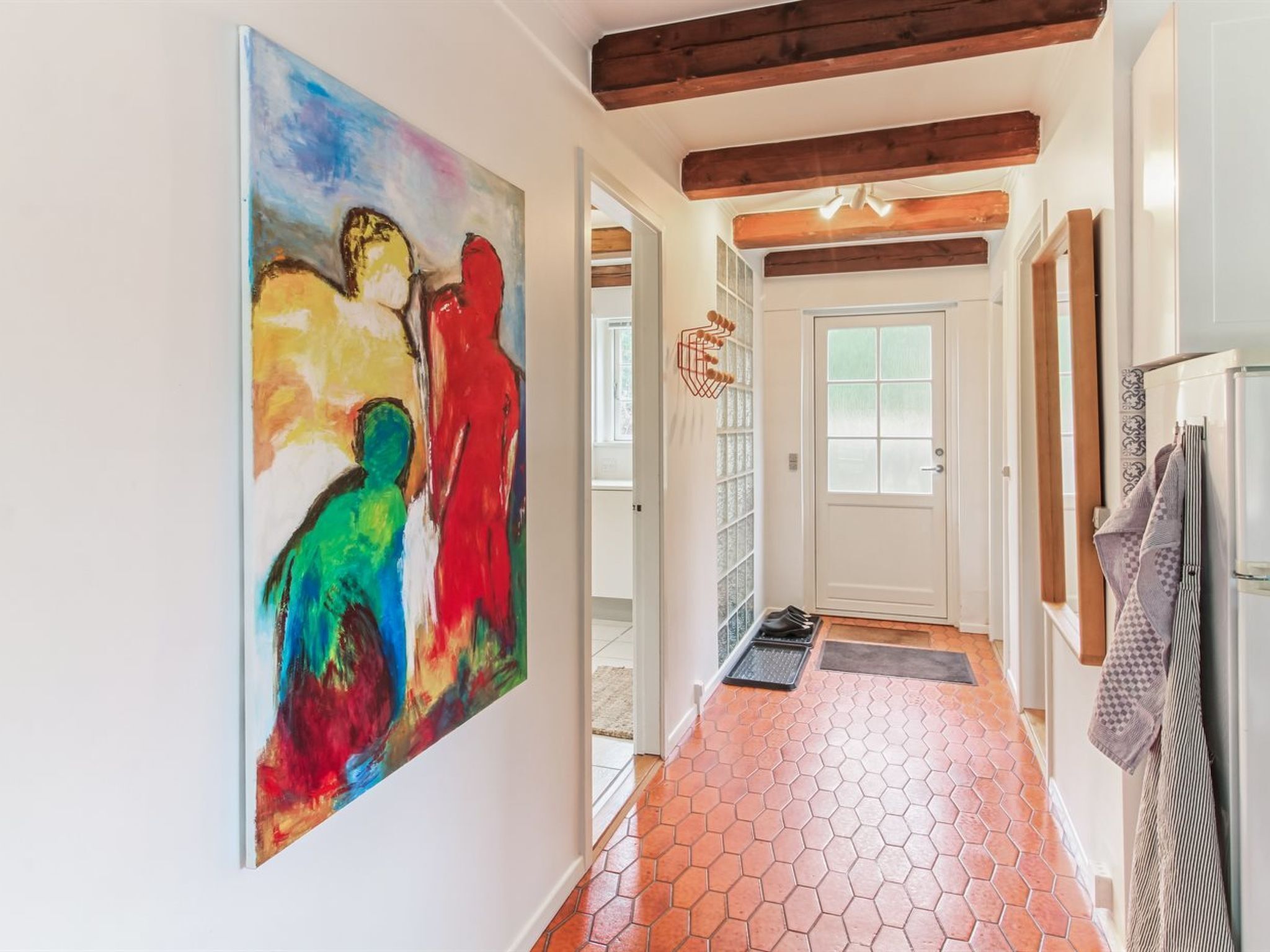 A hallway with a colorful abstract painting on the wall, a hexagonal tiled floor, and a door with a frosted glass panel.