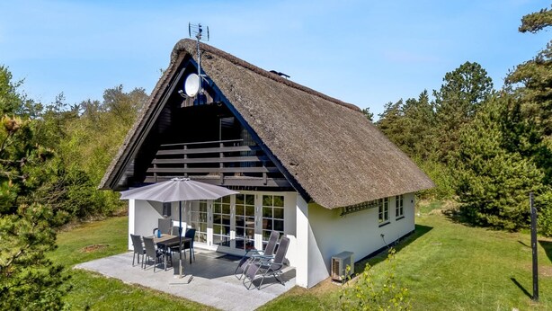 Ein Haus mit Strohdach, einer Terrasse, Sitzgelegenheiten im Freien und einem großen Sonnenschirm.