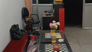 A small, compact living space with a sofa, a coffee table with a chessboard, a small table with a vase of flowers, and a chair.