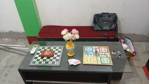 A table with two checkers games, a vase with flowers, and a black bag.