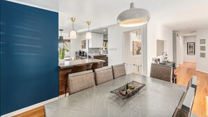 Une cuisine moderne dotée d’un grand îlot central, de luminaires suspendus et d’un coin repas avec une longue table et des chaises rembourrées.